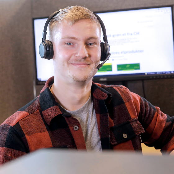 Smilende OK-medarbejder iført headset foran computerskærm