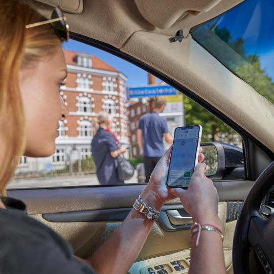 Kvinde sidder i bil med OK's app på smartphones app
