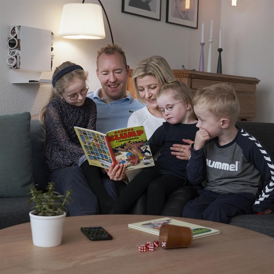 Familie sidder i sofahjørnet og læser Rasmus Klump-bog sammen