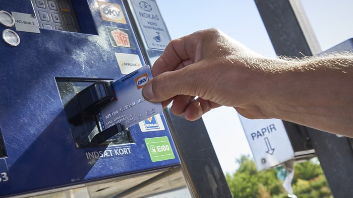 Hånd holder et OK DKV-kort op til en betalingsautomat