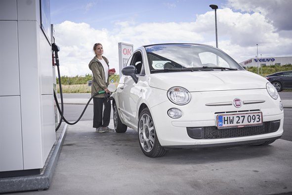 Kvinde tanker lille hvid bil på en OK-tankstation