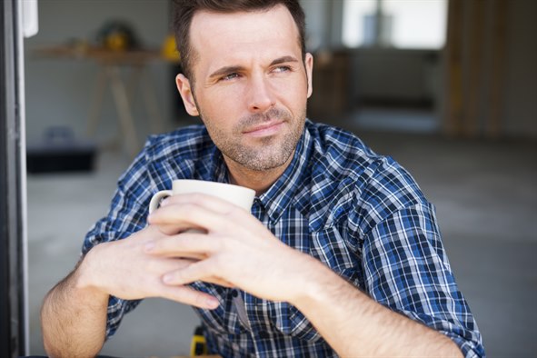 Mand sidder med et kaffekrus og kigger tænksomt ud