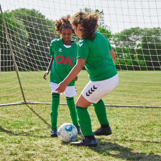 Piger spiller fodbold foran mål