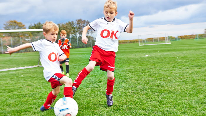 Drenge på fodboldbanen iført fodboldtrøjer med OK-logo på maven