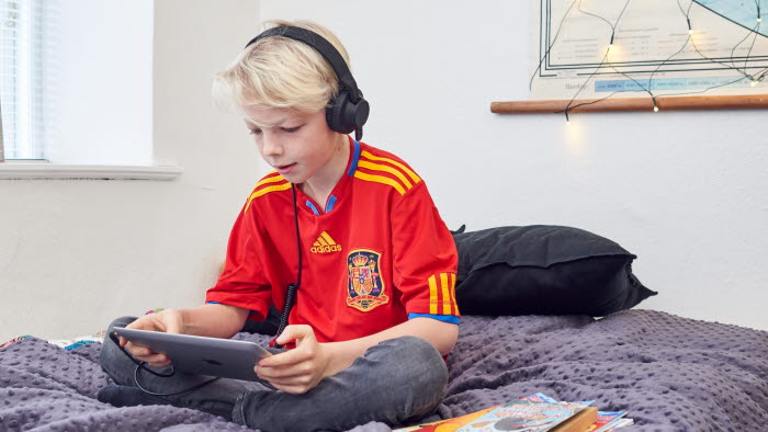 Dreng sidder på seng med tablet og headset