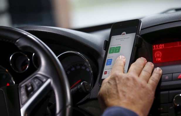 Hånd på mobiltelefon i bil i færd med at vælge bilvask med OK-appen