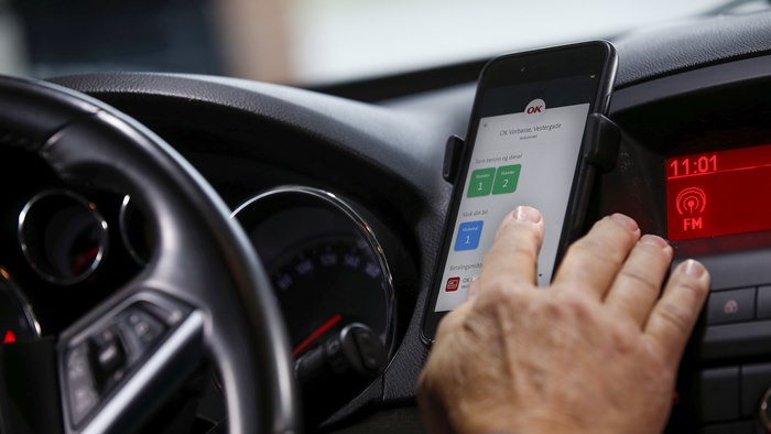 Hånd på mobiltelefon i bil i færd med at vælge bilvask med OK-appen