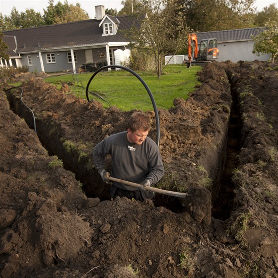 Mand i færd med at grave op til jordvarme i haven ved et hus