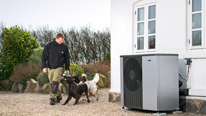 Mand går med hunde ved siden af hus med varmepumpe