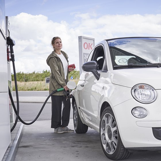 Kvinde tanker lille hvid bil på en OK-tankstation