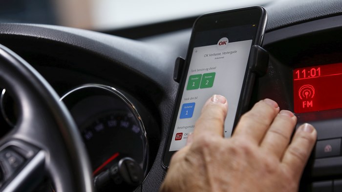 Hånd på mobiltelefon i bil i færd med at vælge bilvask med OK-appen