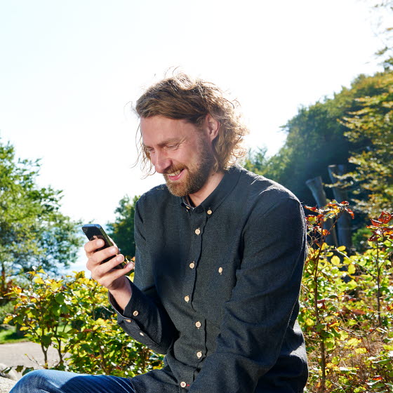 Ung mand sidder ude og kigger på mobiltelefon