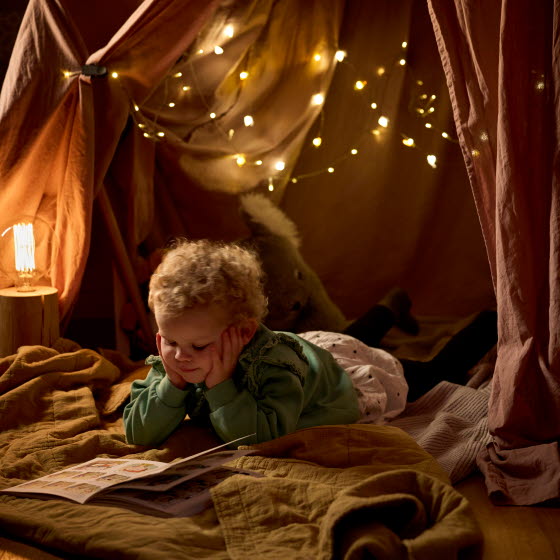 Barn læser i en hule med hyggelig belysning