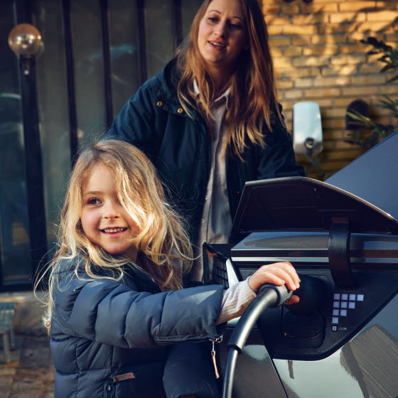 Pige med ladestik til elbil i hånden ved siden af bilen