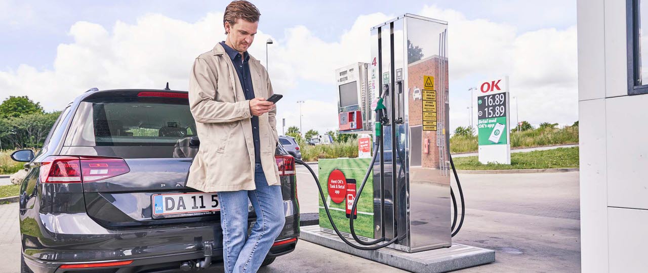 mand står op af sin bil på tanken med sin telefon