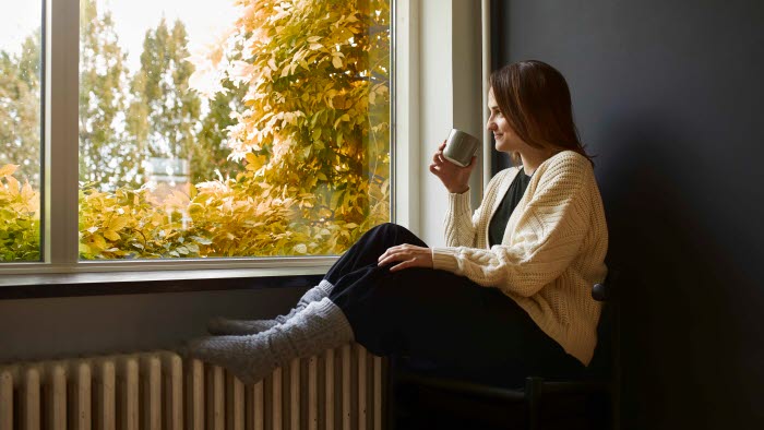 Kvinde sidder i vindueskarm med fødder på radiator