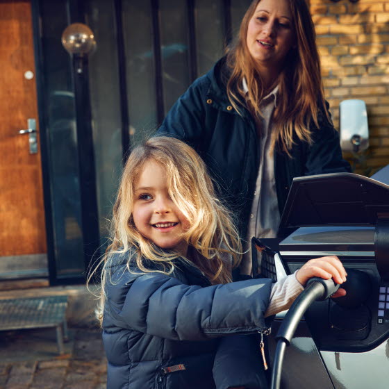 Pige med ladestik til elbil i hånden ved siden af bilen