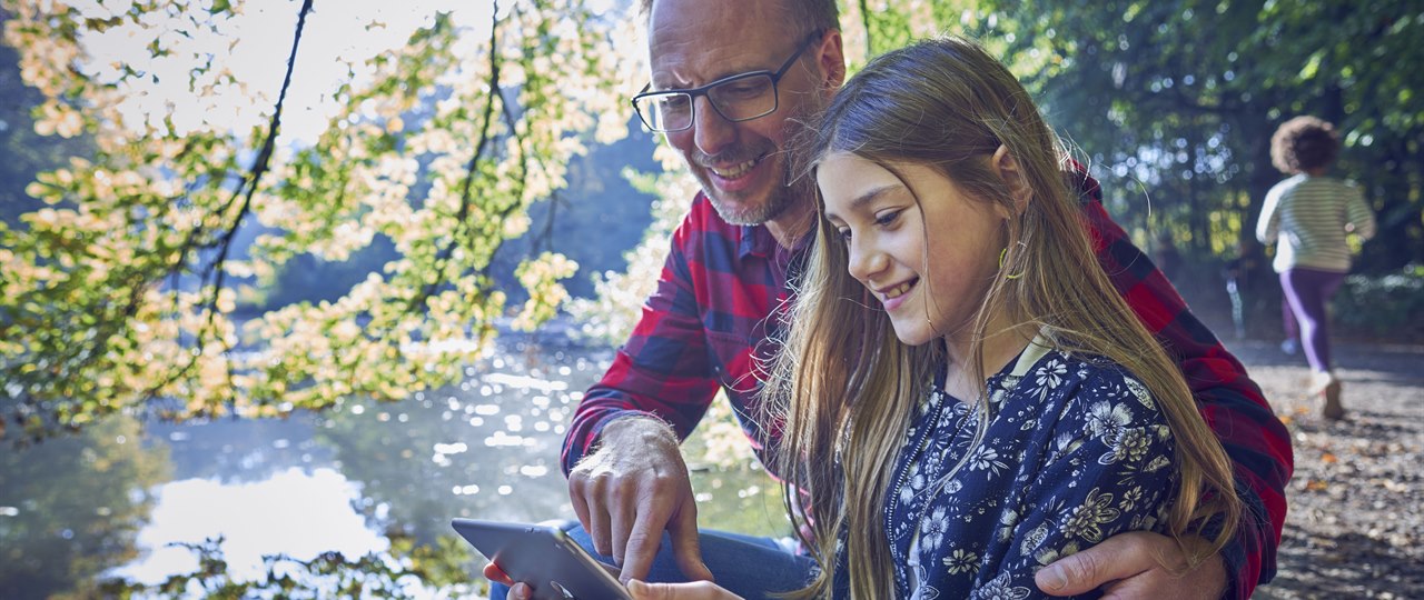 Far og datter i skoven sidder med tablet