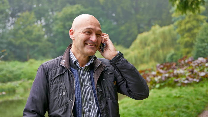 Mand taler i mobiltelefon med grønt område i baggrunden
