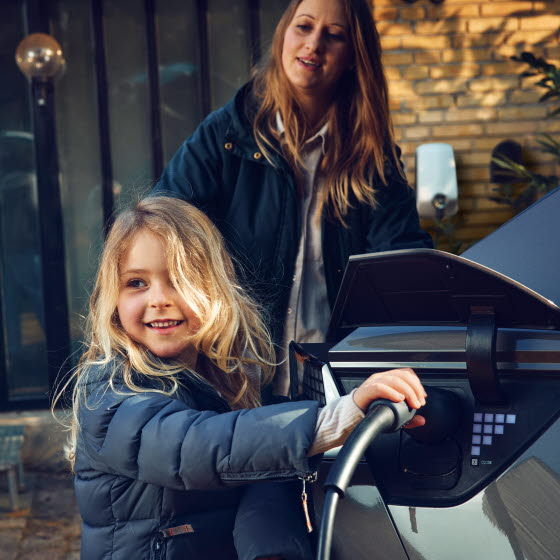 Pige med ladestik til elbil i hånden ved siden af bilen