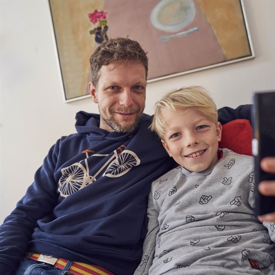 Far og søn sidder tæt sammen i sofa med mobiltelefon foran sig