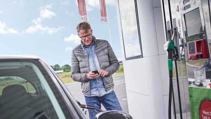 Mand i færd med at tanke brændstof på OK-tankstation mens han holder sin mobiltelefon