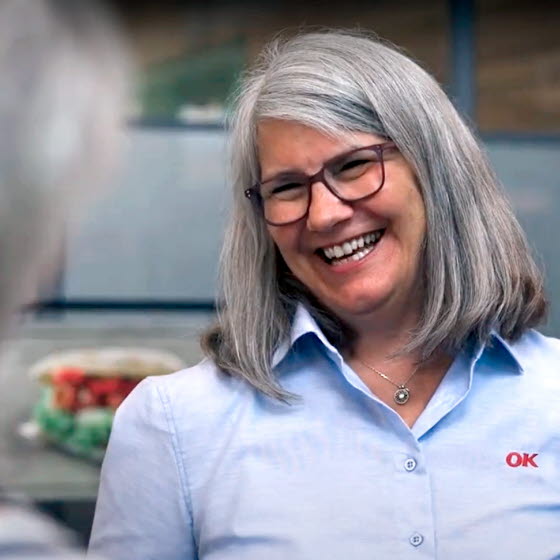 Smilende kvinde med OK-logo på skjorten