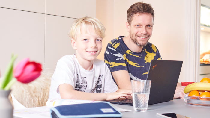 Far og søn ved spisebord med PC og penalhus foran sig