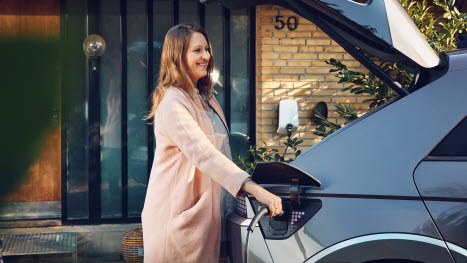 Kvinde står med ladestik til elbil ved bilen