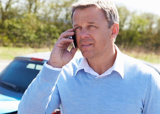 Mand står ved siden af mindre biluheld og taler i mobiltelefon