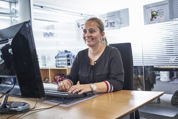 Smilende kvinde sidder på kontor foran computerskærm og tastatur