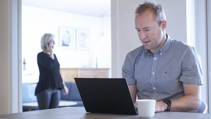 Mand sidder med bærbar computer ved spisebord