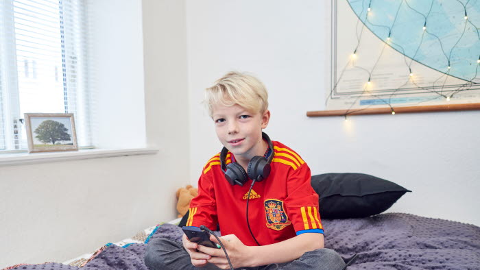 Dreng sidder på seng med mobiltelefon og headset