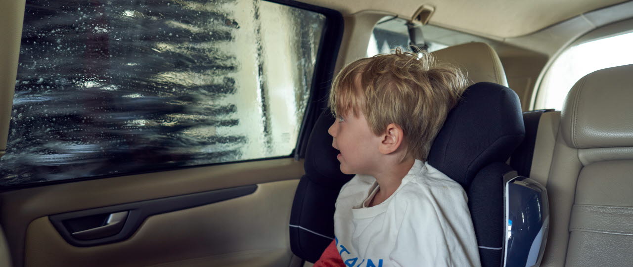 Dreng sidder i barnesæde i bilen under en bilvask i en af OK's vaskehaller