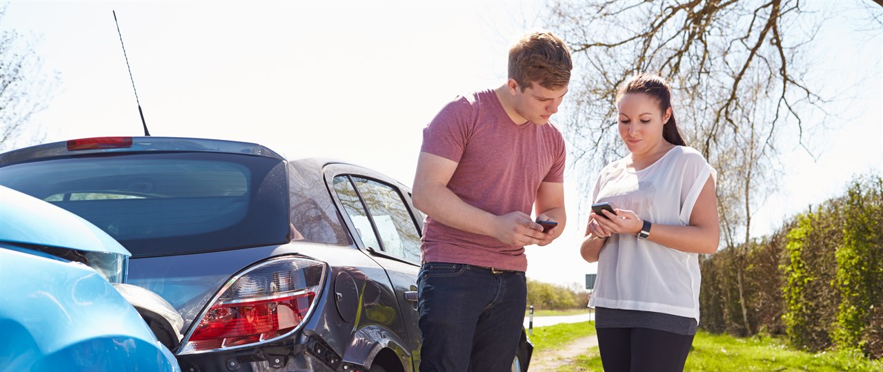 En mand og en kvinde står ved siden af to biler og udveksler information