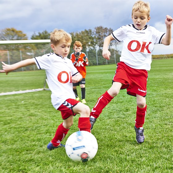 Drenge på fodboldbanen iført fodboldtrøjer med OK-logo på maven