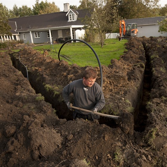 Mand i færd med at grave op til jordvarme i haven ved et hus