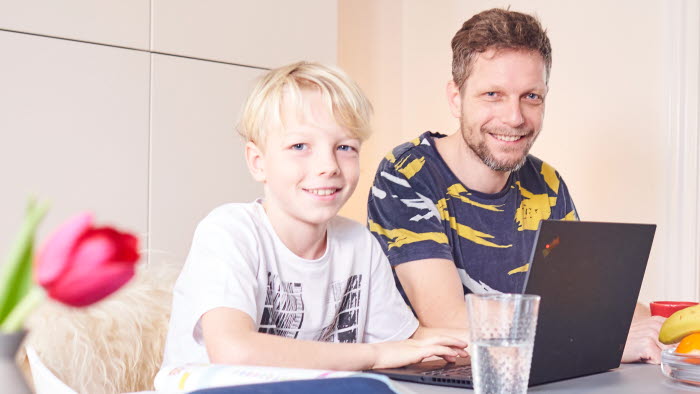 Far og søn ved spisebord med PC og penalhus foran sig