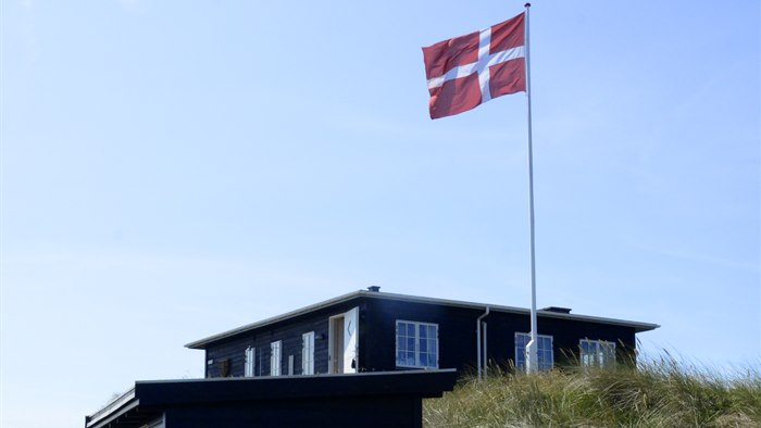Sommerhus med flagstang og Dannebrogsflag på blå sommerhimmel