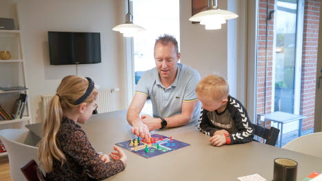 Far med to børn spiller ludo ved spisebord