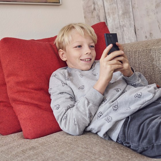 Dreng ligger på sofaen og kigger på mobiltelefon