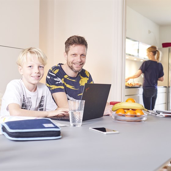 Far og søn ved spisebord med PC og penalhus foran sig