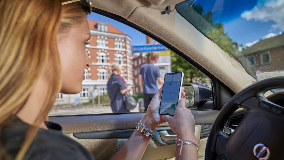 Kvinde sidder i bil med OK's app på smartphones app