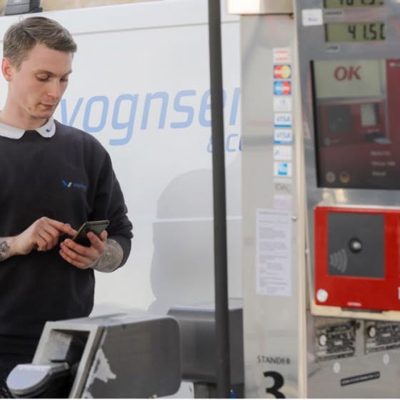 Mand kigger på telefon ved tankstation