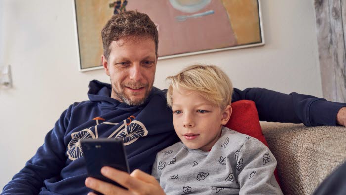 Far og søn sidder sammen i sofa og kigger på en mobiltelefon