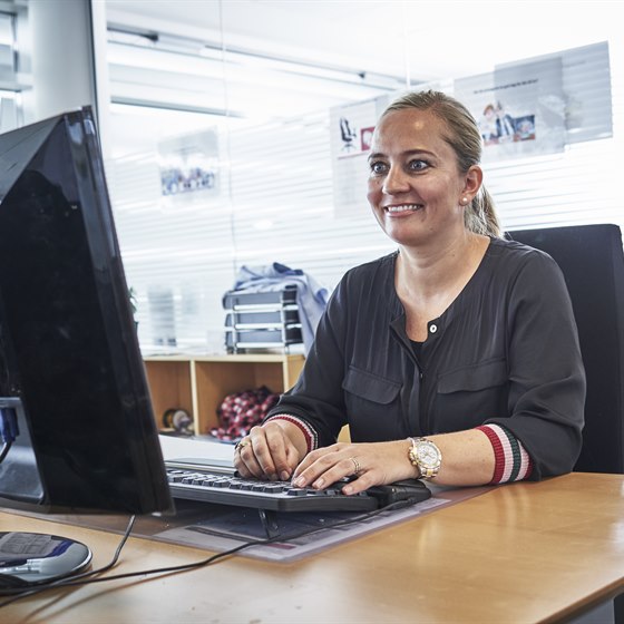 Smilende kvinde sidder på kontor foran computerskærm og tastatur