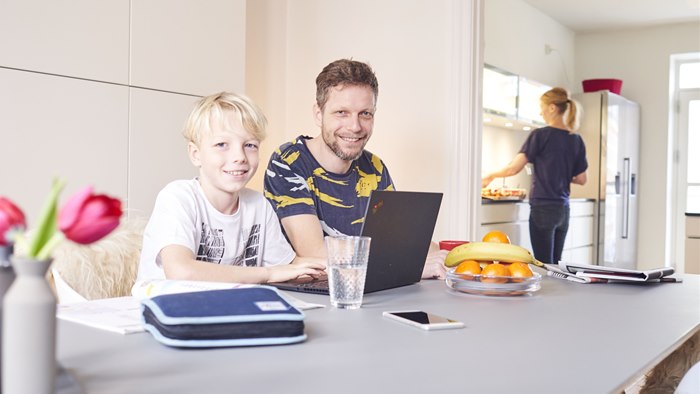 Far og søn ved spisebord med PC og penalhus foran sig