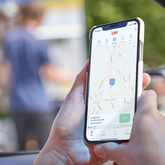 Kvindehånd holder telefon med parkering i OK-appen