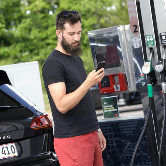 Mand med mobiltelefon på tankstation