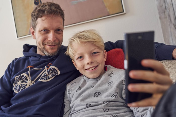 Far og søn sidder tæt sammen i sofa med mobiltelefon foran sig